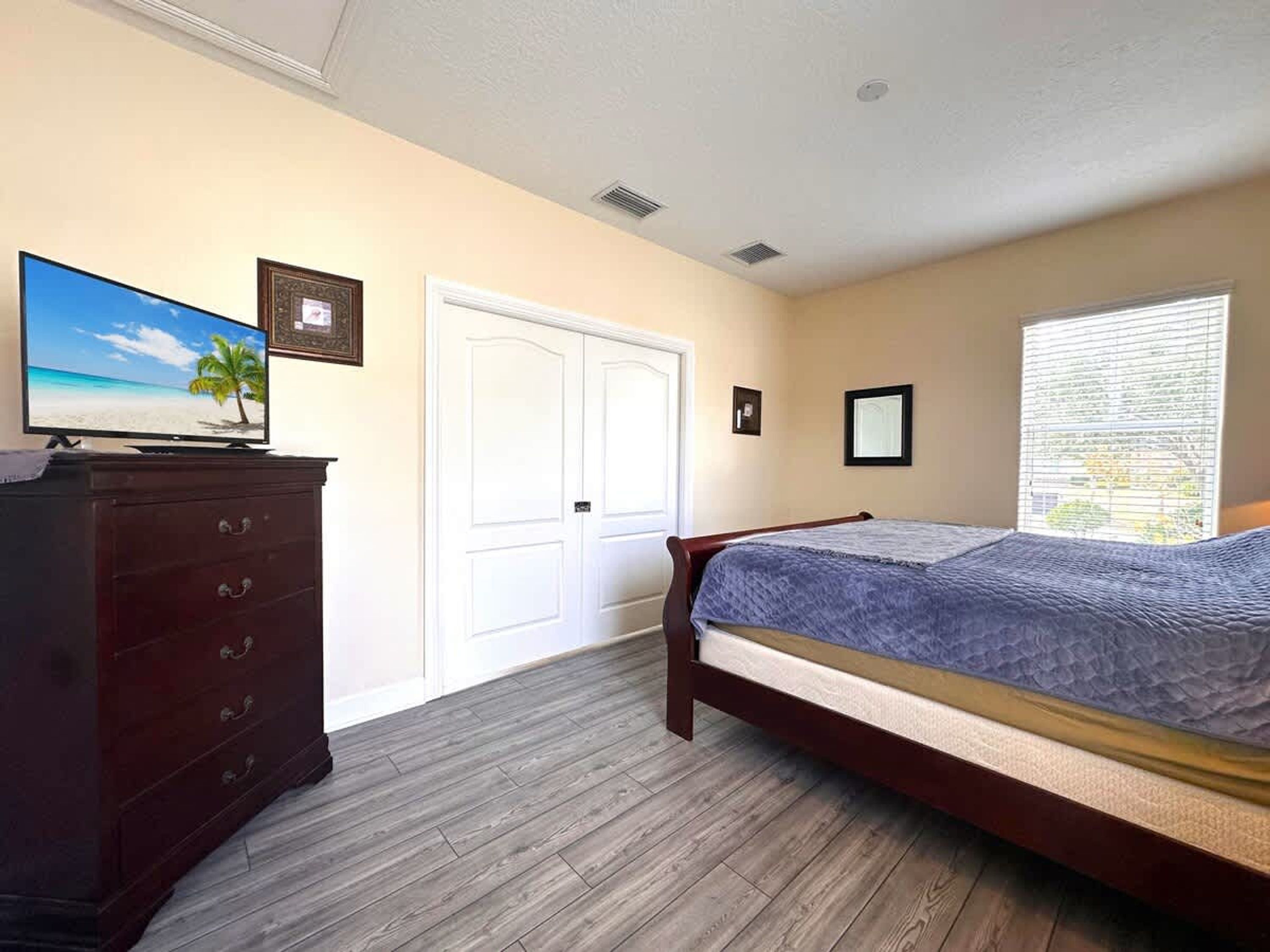 A bedroom with a bed, dresser, TV, and a door.