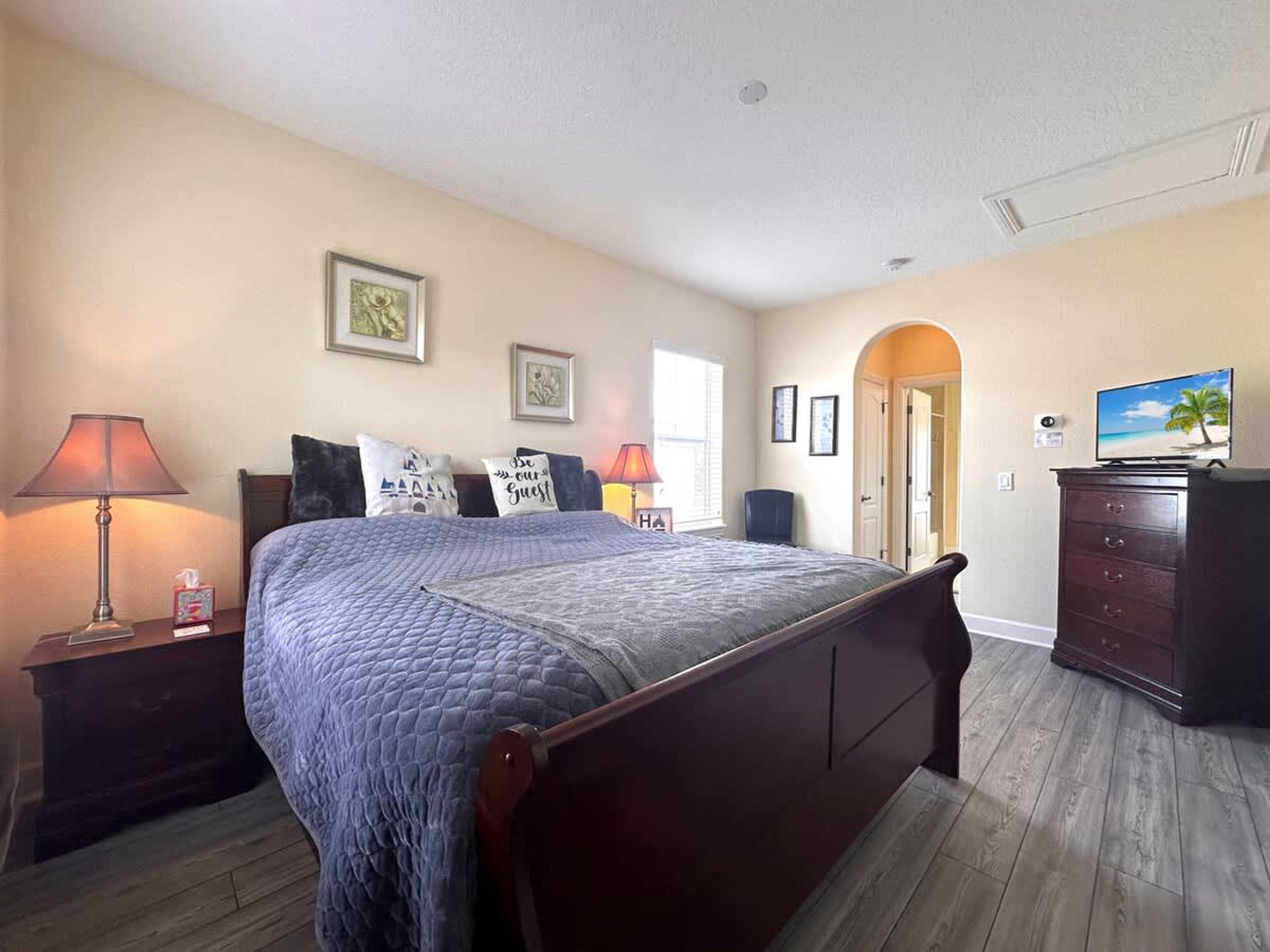 A bedroom with a large bed, a nightstand with a lamp, a dresser, and a television on a dresser.