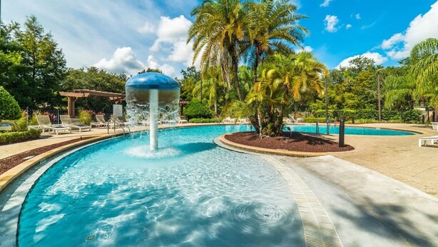 A swimming pool with a water fountain, surrounded by palm trees and lounge chairs. - 4Bd Minions Themed Home Near Disney Sleeps 10 (Kissimmee)