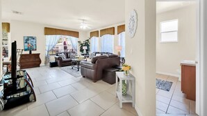A spacious living room with a brown leather sofa, a coffee table, and a dining area with a glass table and chairs.
