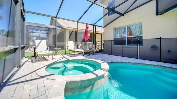 A swimming pool with a hot tub, surrounded by lounge chairs and a glass enclosure.