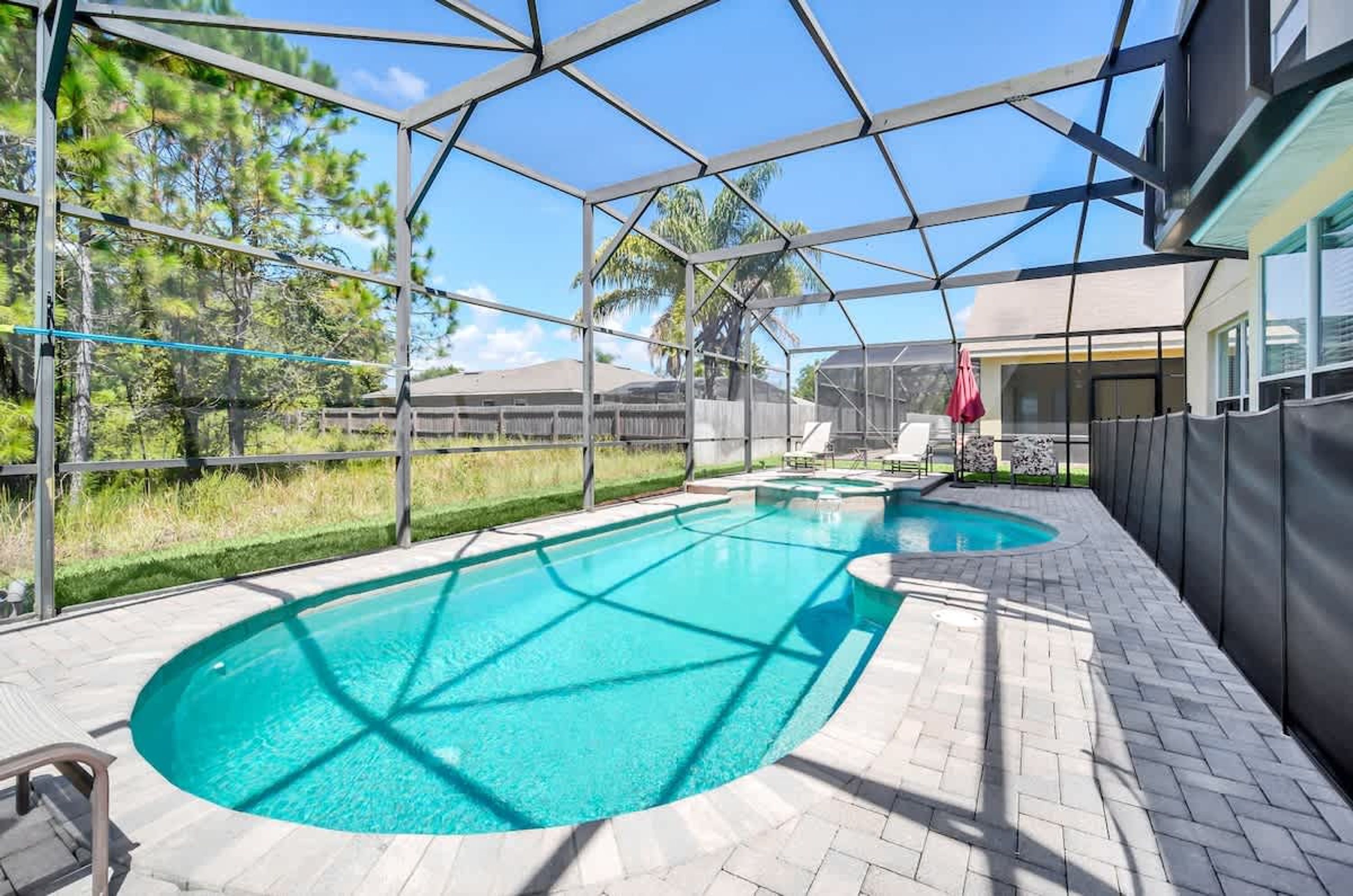 An outdoor swimming pool with a clear blue water feature, surrounded by a covered patio area with a view of the surrounding landscape.