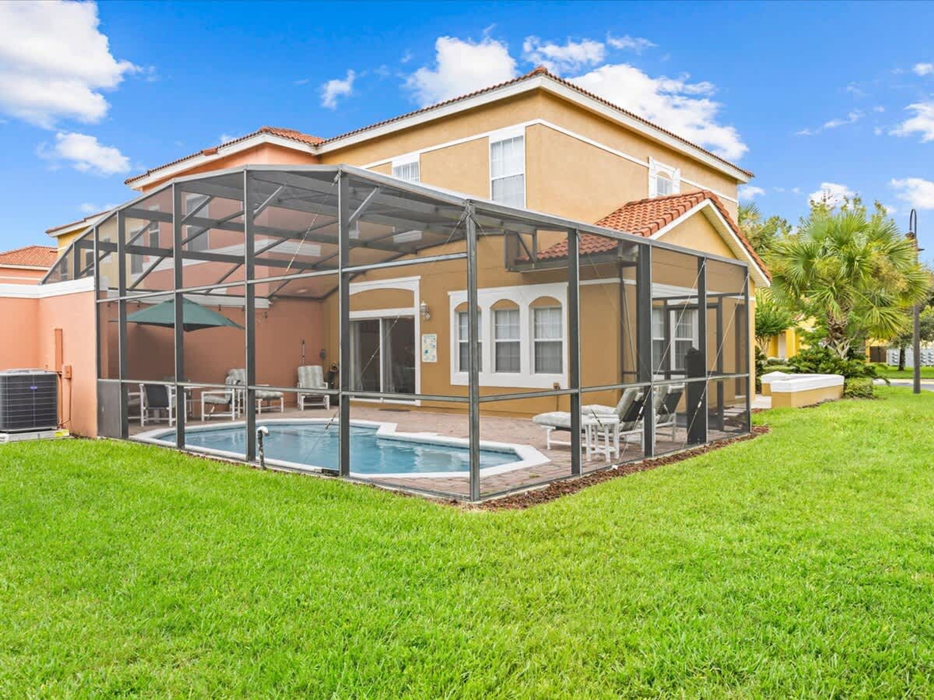 A house with a covered outdoor pool area, a patio with chairs, and a lawn.