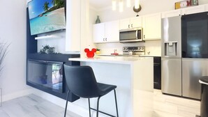 Een moderne keuken met witte kastjes, een roestvrijstalen koelkast, een magnetron en een groot kookeiland met een barkruk.