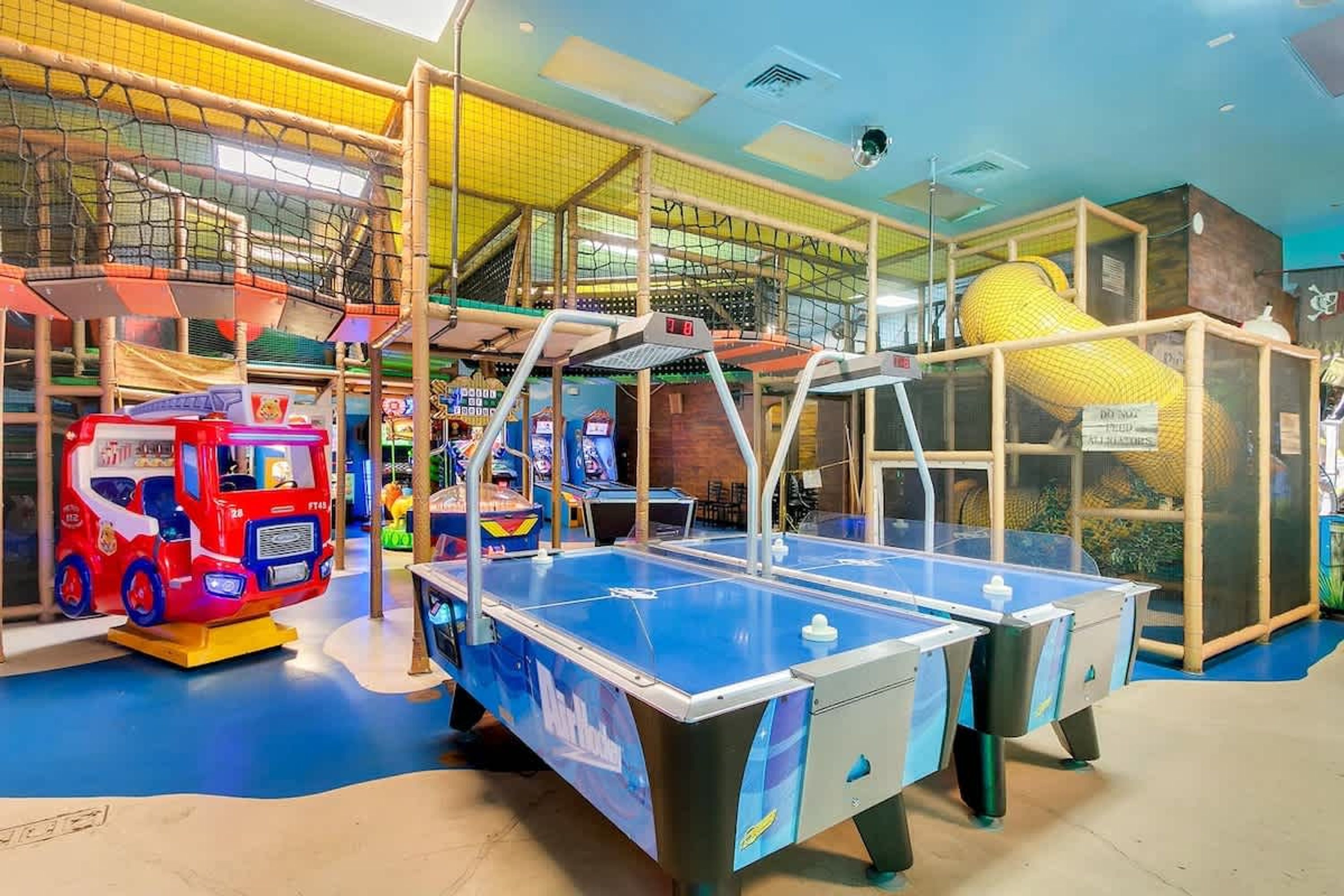 Un área de juegos interior con mesa de ping pong, un camión de bomberos de juguete rojo y un tobogán amarillo.