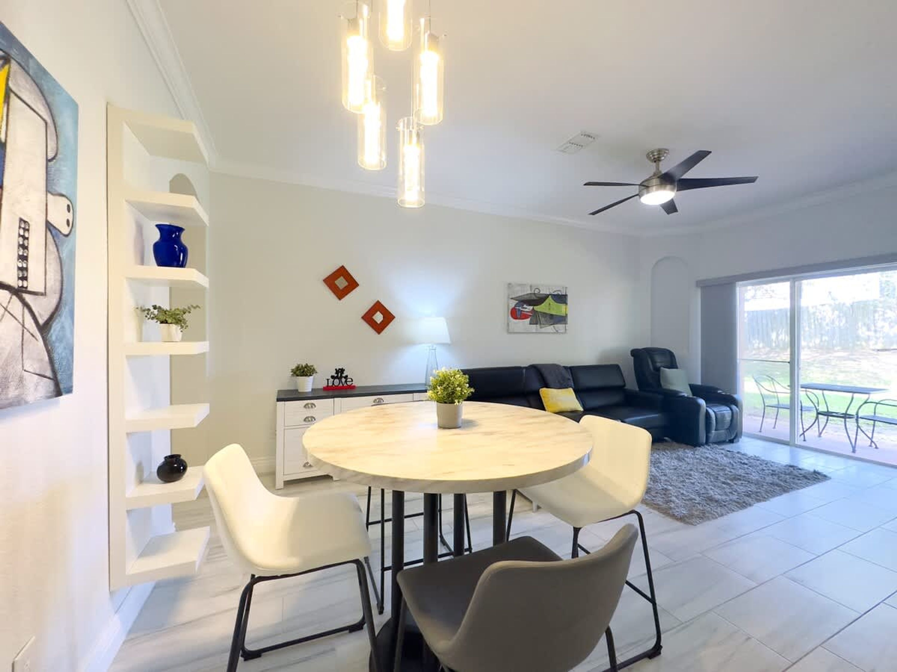 A modern living room with a round dining table, white chairs, a black sofa, and a ceiling fan.