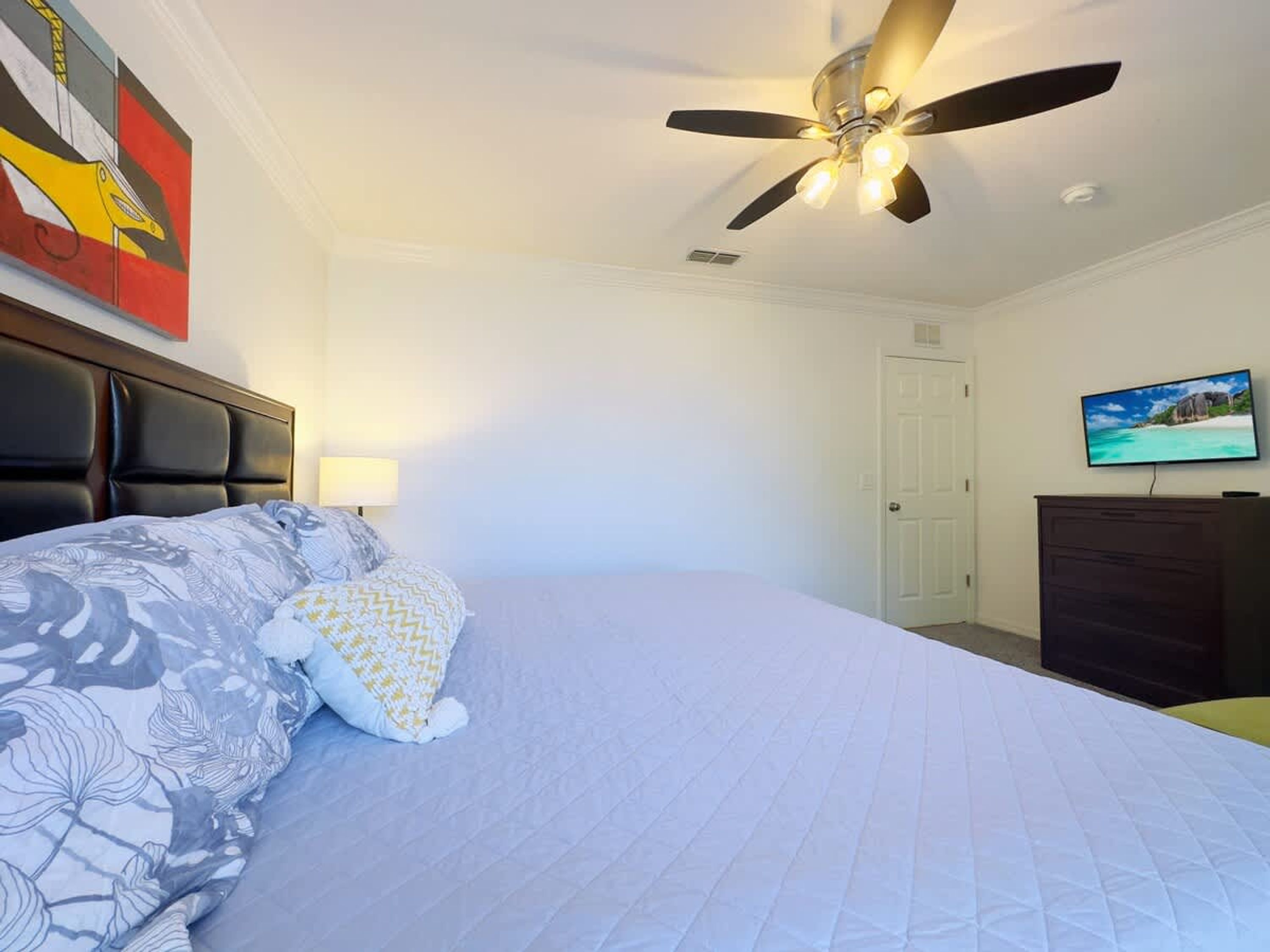 Un dormitorio con cama, ventilador de techo, televisión y una puerta.