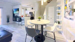 Een moderne keuken met witte kastjes, een eethoek met een ronde tafel en stoelen, en een plafondventilator.
