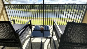 A balcony with a table and two chairs, overlooking a body of water and grassy area. - Very Near Disney 3 Bd Condo Walmart 1 min Away (Kissimmee)