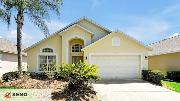 A single-story house with a garage, a small front yard with a palm tree and shrubs, and a clear blue sky.