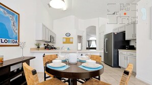 A modern kitchen with white cabinets, a black refrigerator, and a dining area with a round table and wicker chairs.