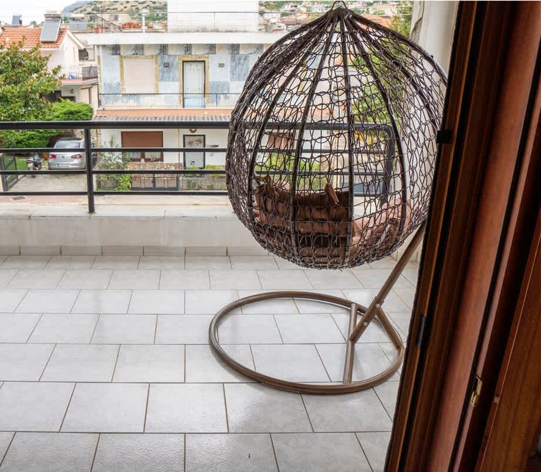 A balcony with a hanging chair, a view of the neighborhood, and a tiled floor.