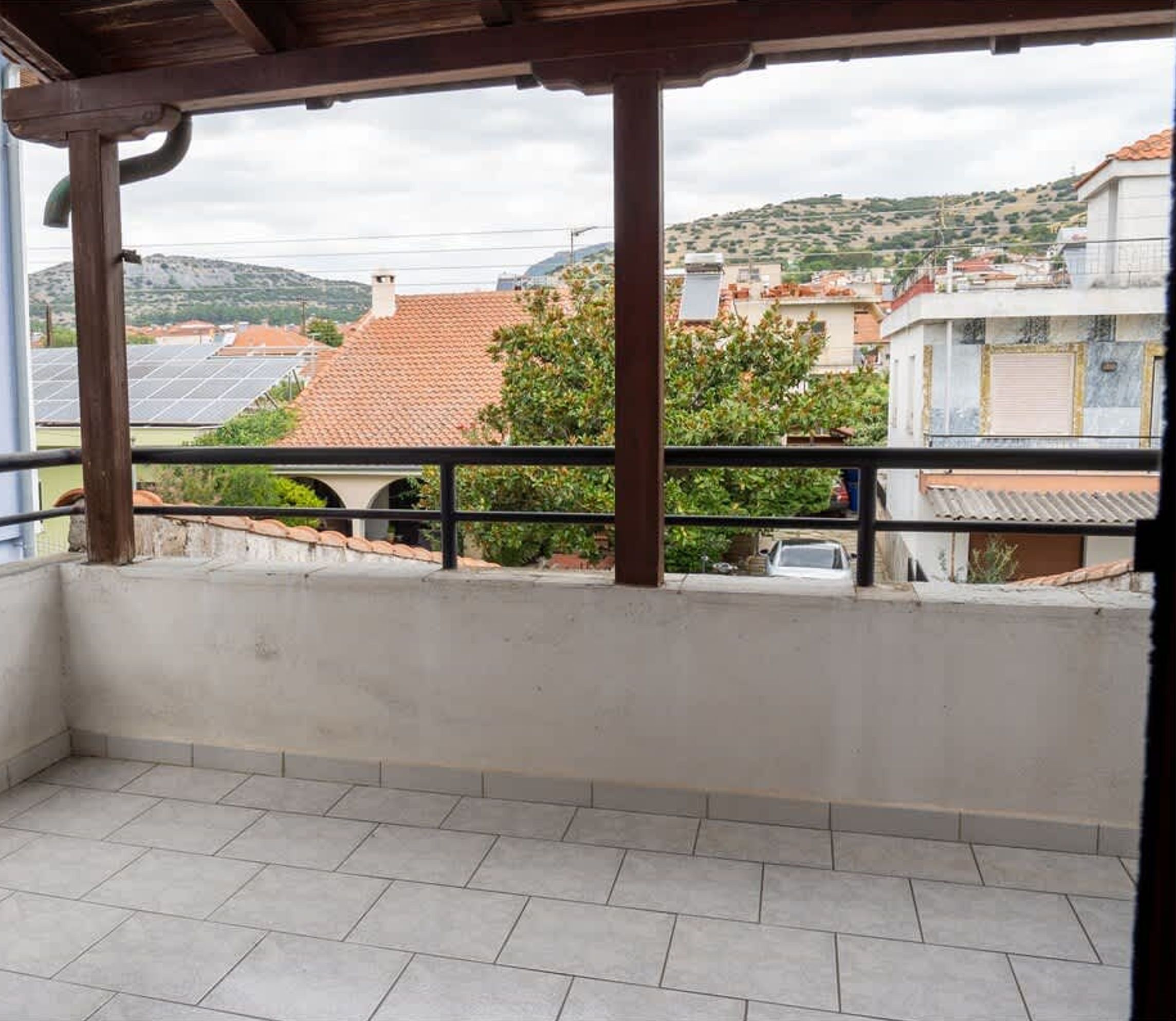 A balcony with a tiled floor and a view of buildings and hills in the background.