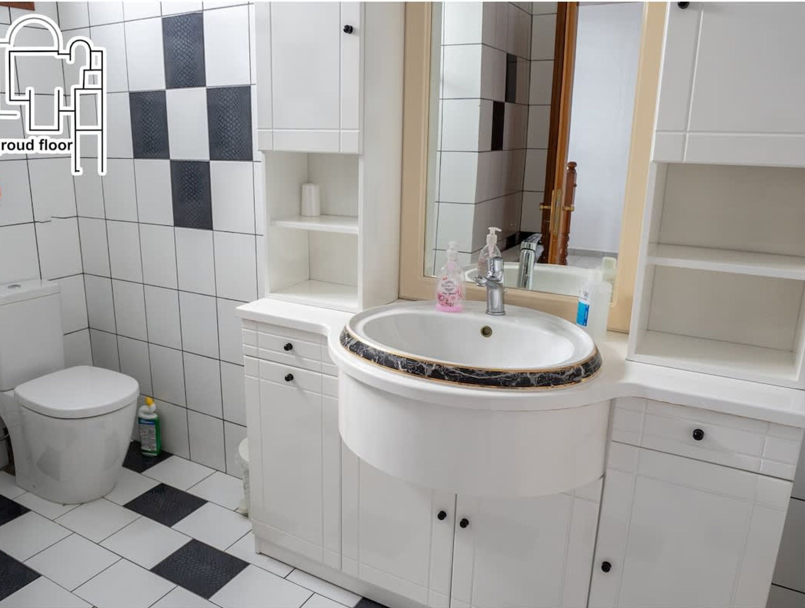 Un baño con inodoro, lavabo y espejo. El suelo presenta un estampado de cuadros y las paredes son blancas.