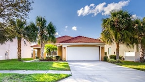 A residential house with a red-tiled roof, a garage, and a well-maintained lawn with palm trees.