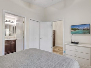 Een slaapkamer met een bed, een dressoir, een televisie en een badkamer met spiegel en wastafel.