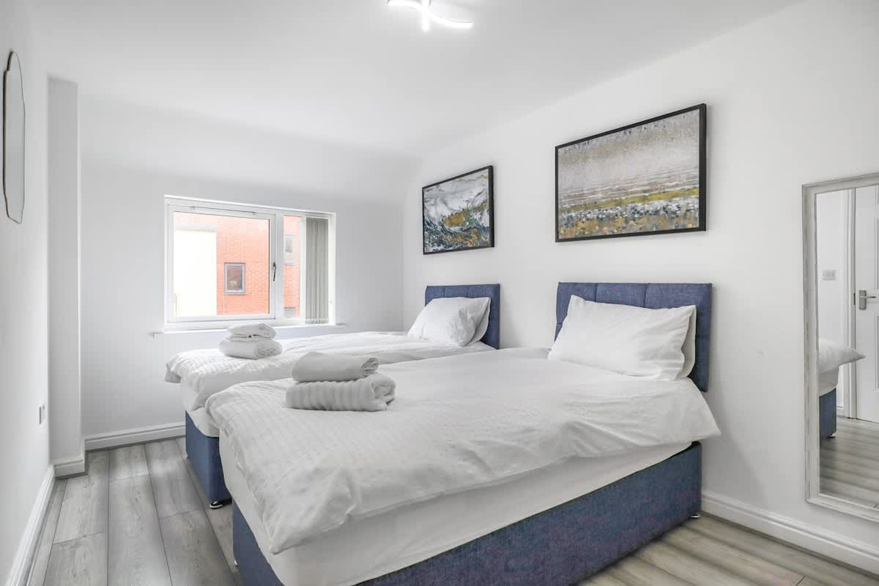 Ein modernes Hotelzimmer mit zwei Betten, einem großen Fenster und Bildern an der Wand.