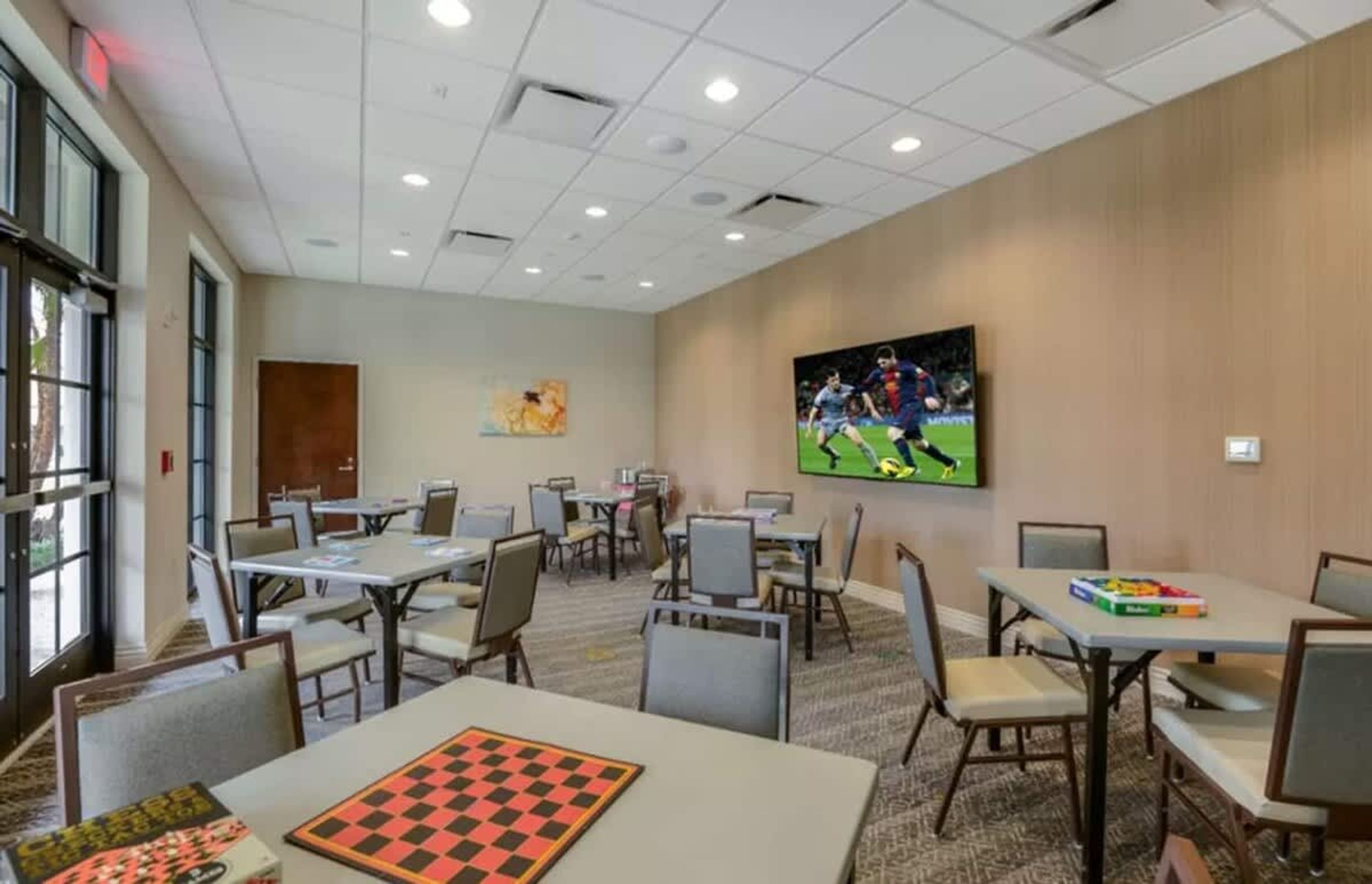 A conference room with tables, chairs, a large screen, and a door.
