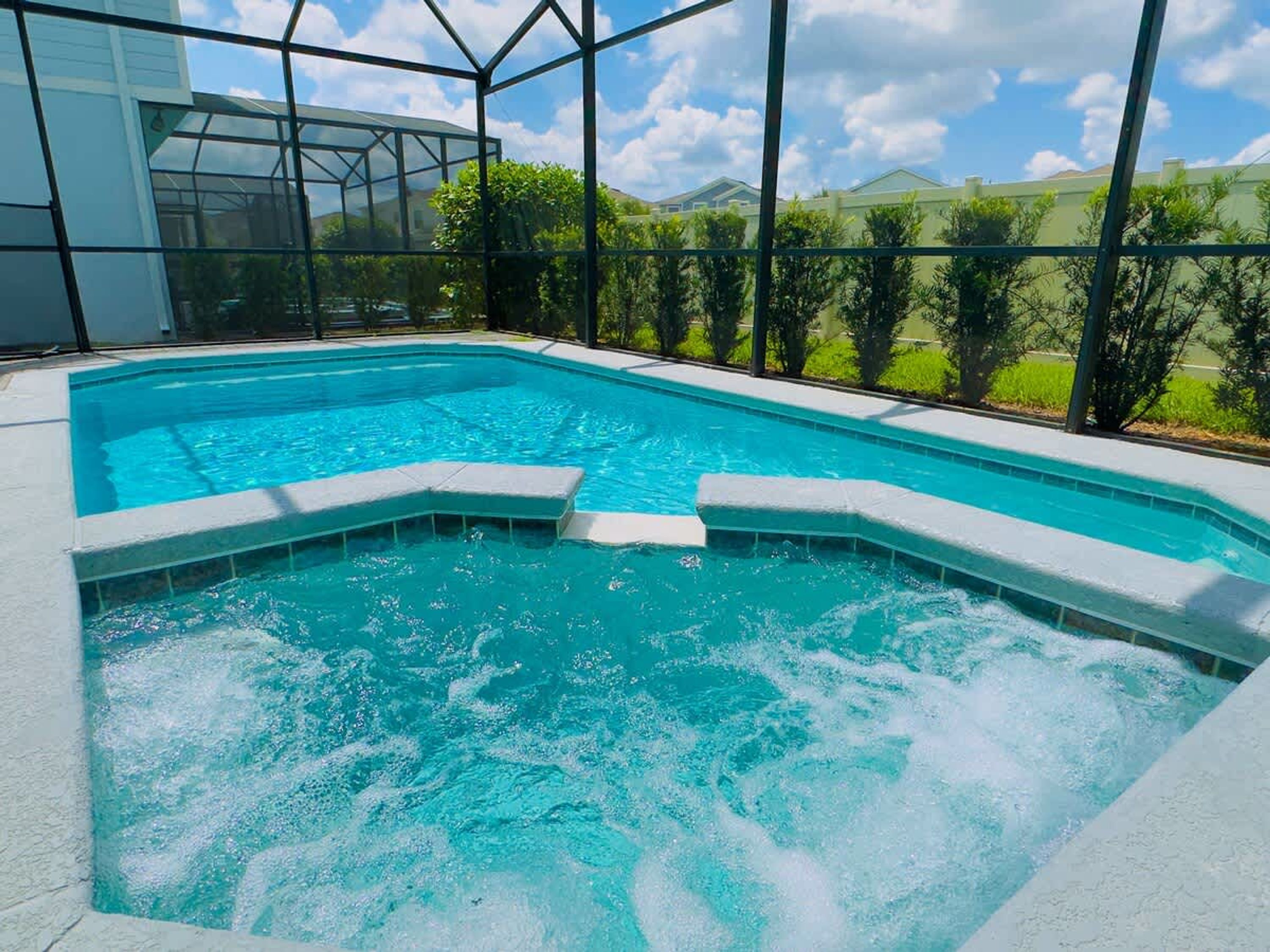 En swimmingpool med en glasvägg runt om, omgiven av grönska och en klar himmel.