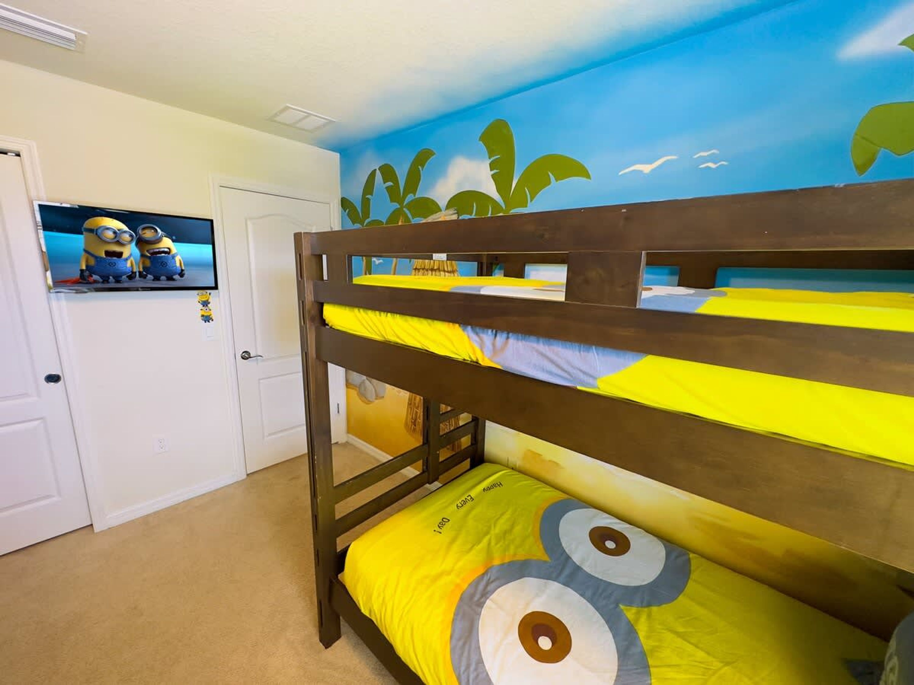 A bunk bed with a Minion-themed mattress and wall art, a television on the wall, and a door with a white frame.