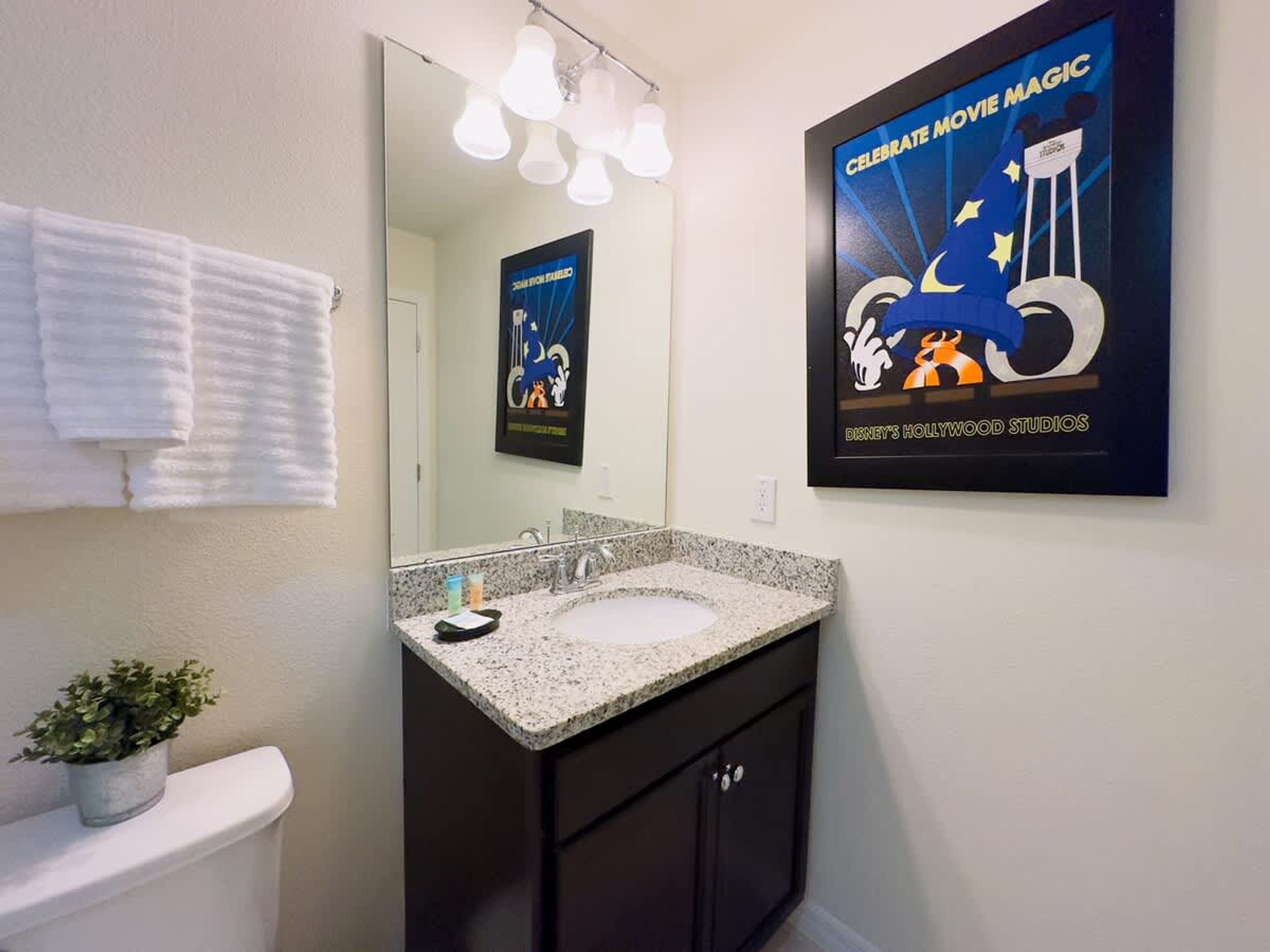 A bathroom with a white sink, dark cabinets, a mirror, and a poster of 'Celebrate Movie Magic' at Disney's Hollywood Studios.