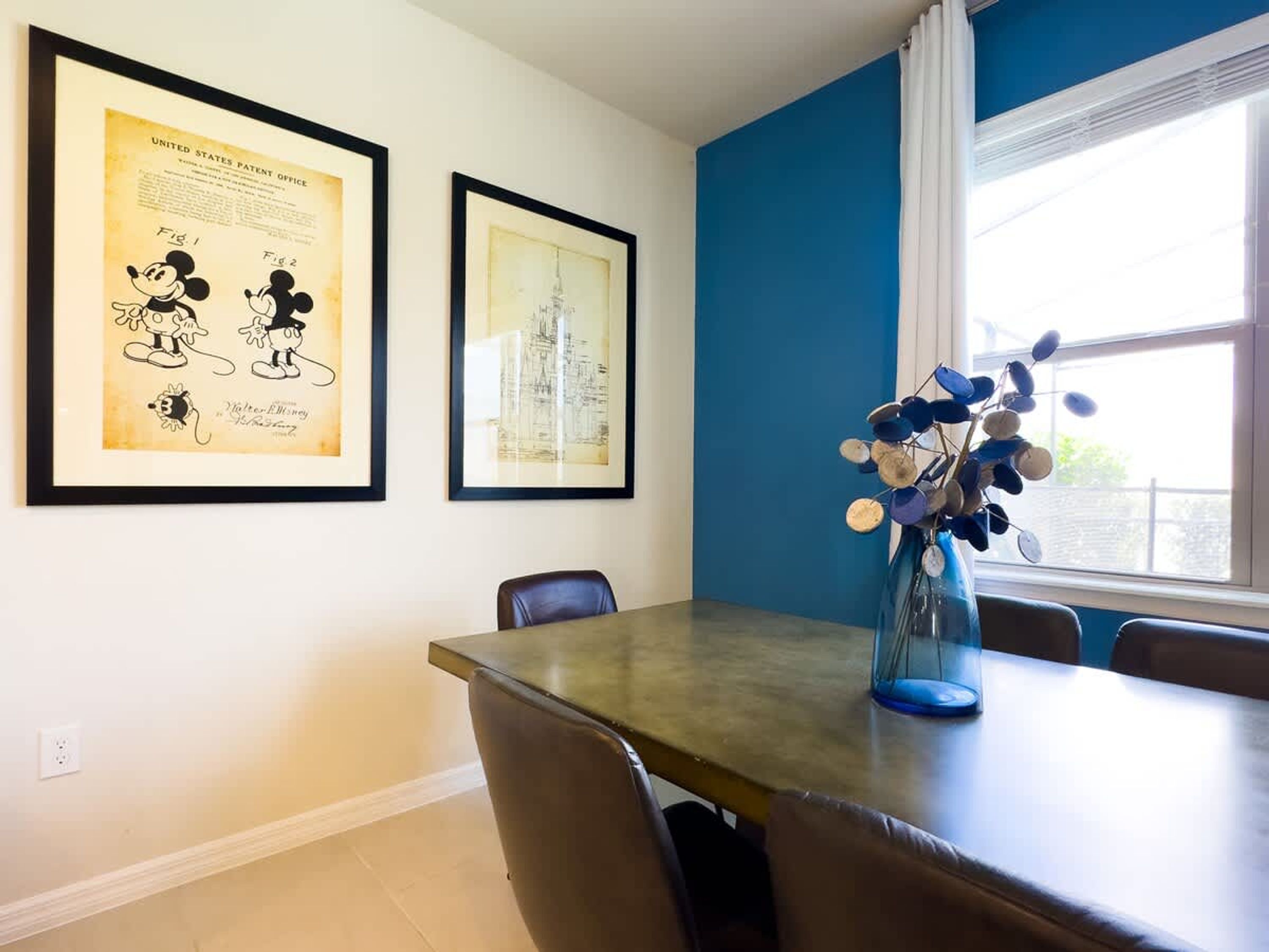 A dining area with a table, chairs, and framed artwork on the wall.
