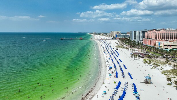A beach with a pier extending into the ocean, lined with blue umbrellas and beach chairs. - 445 Clearwater Hamden (Clearwater Beach)