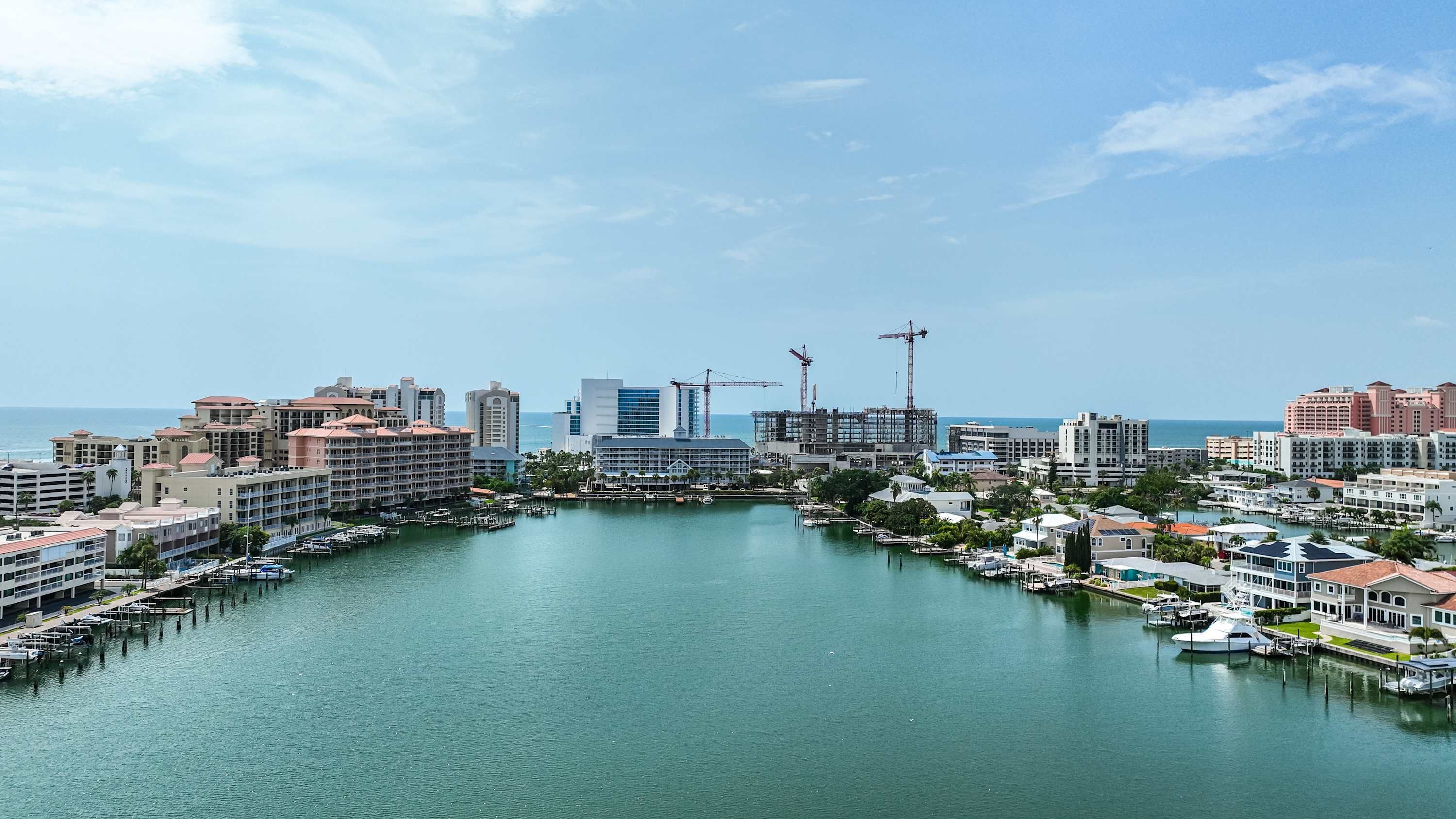 Puerto deportivo con barcos amarrados, rodeado de edificios y grúas de construcción.