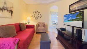 A living room with a red sofa, a patterned armchair, a small table, a TV, and a wall decoration. - 4Bd Pool Villa in Calabay Parc Close to Disney Sleeps 8 (Haines City)