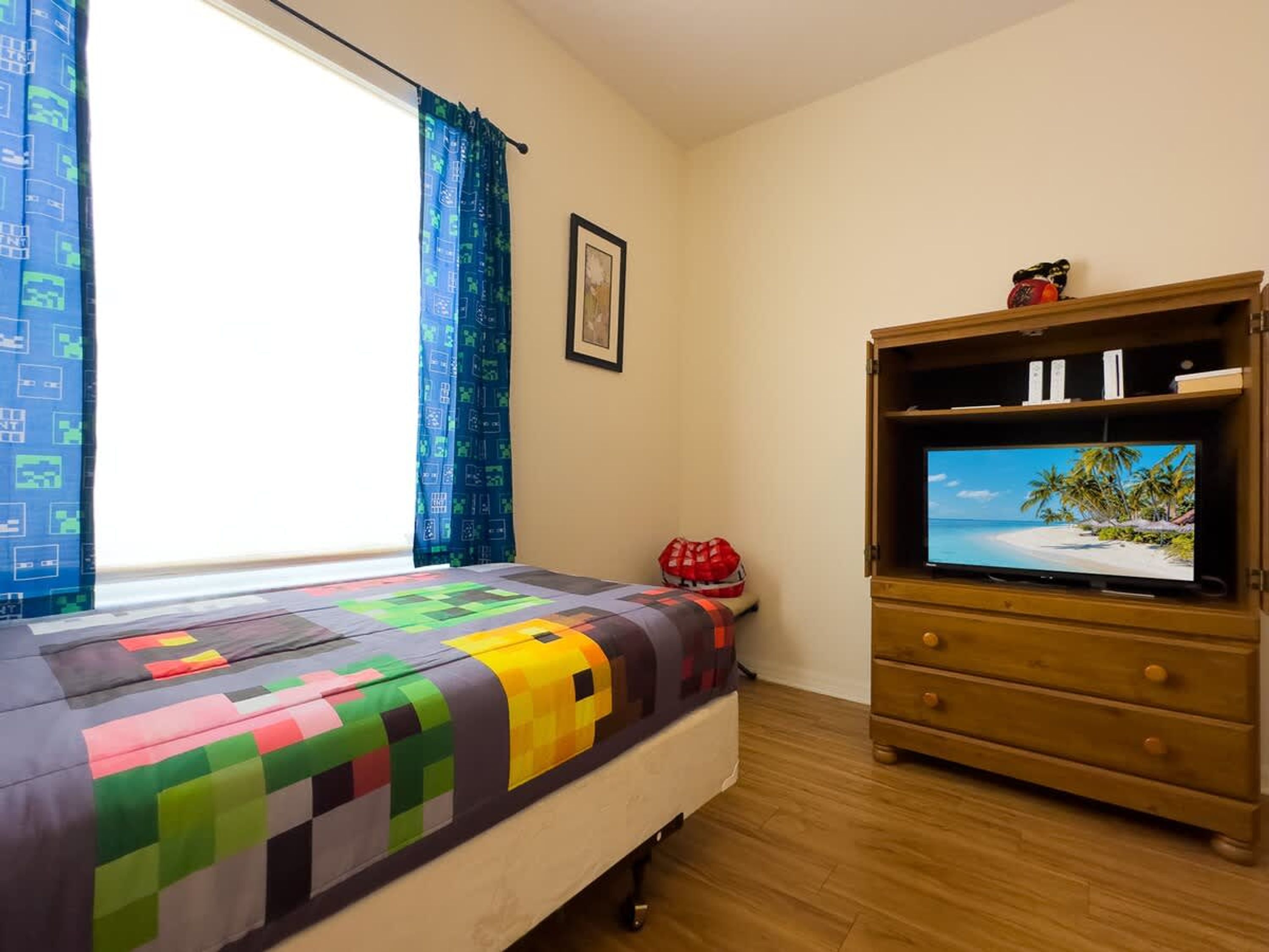 Un dormitorio con una cama, un televisor sobre un mueble de madera y una ventana con cortinas.