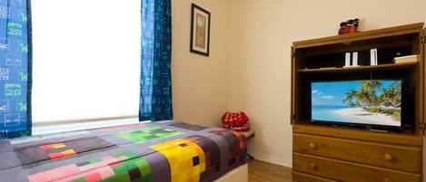 Un dormitorio con una cama, un televisor sobre un mueble de madera y una ventana con cortinas.
