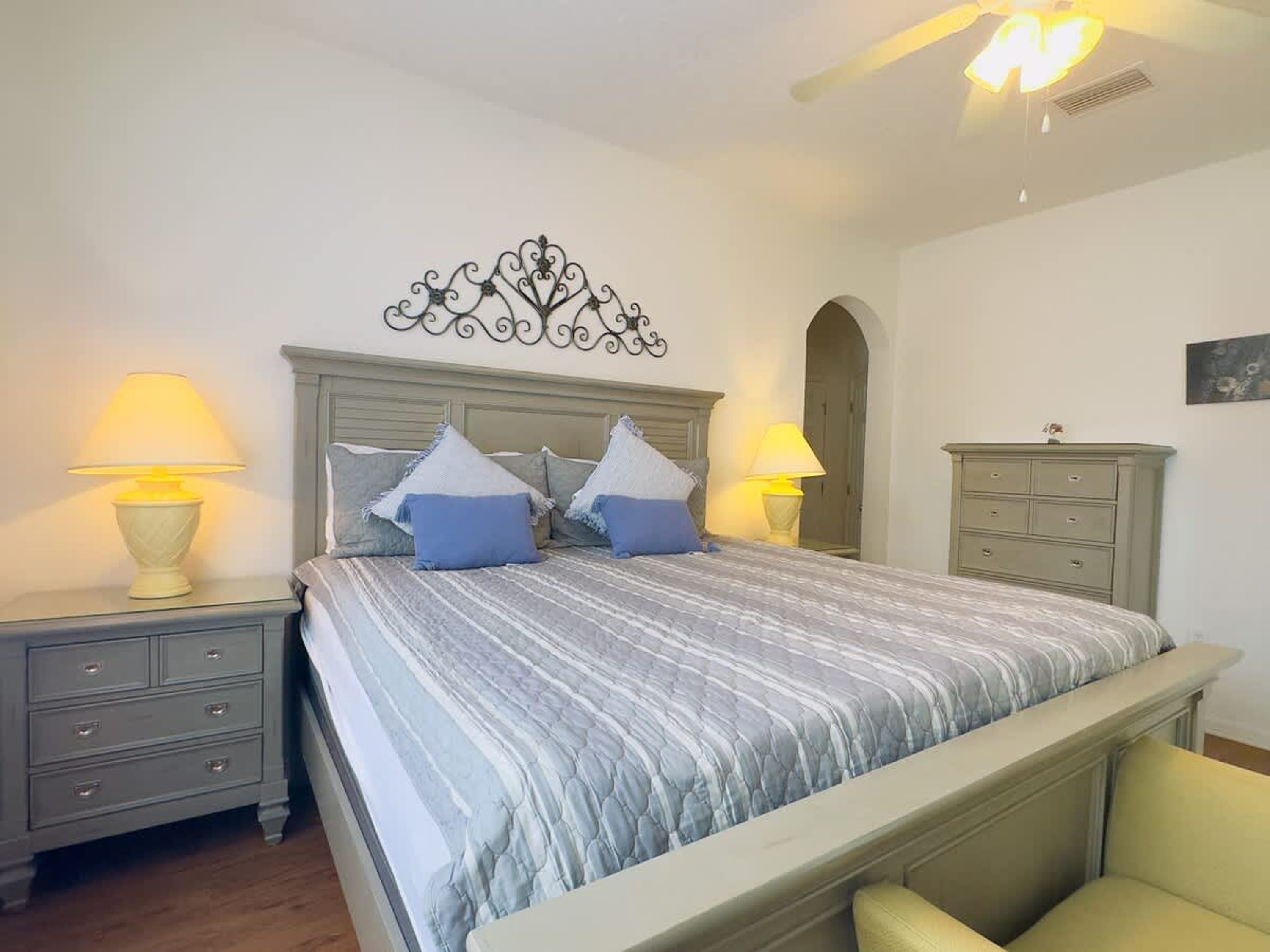 A bedroom with a bed, two bedside tables with lamps, a dresser, and a decorative wall piece.