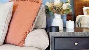 A living room with a beige sofa, a peach throw blanket, a vase with flowers, and a small table with a black object and a white container. - 4BR Charming Oasis With King Beds (Kissimmee)