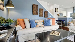 A modern living room with a white sofa set, a black coffee table, and a staircase leading to the upper floor. - 4BR Charming Oasis With King Beds (Kissimmee)