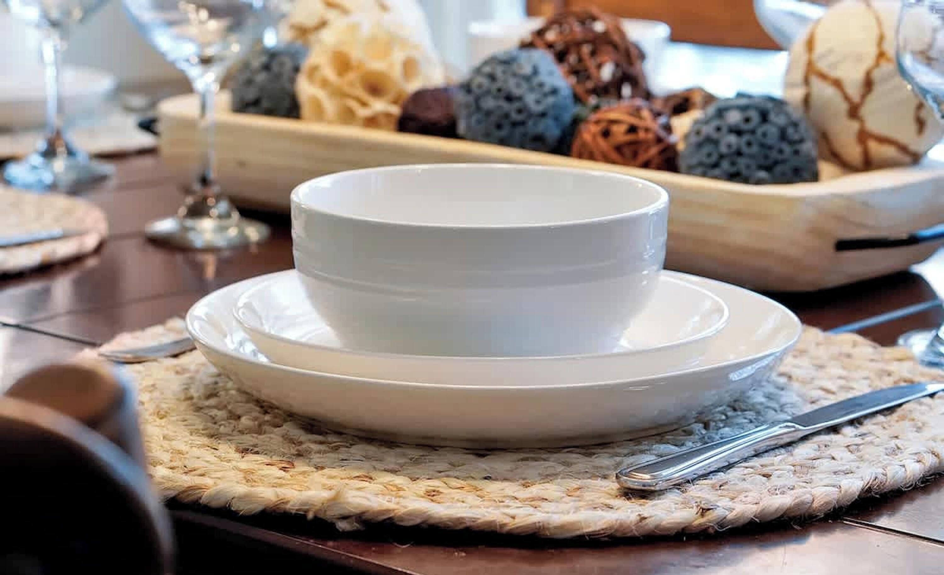 A dining table with a white bowl set on a woven placemat, accompanied by a knife and spoon.