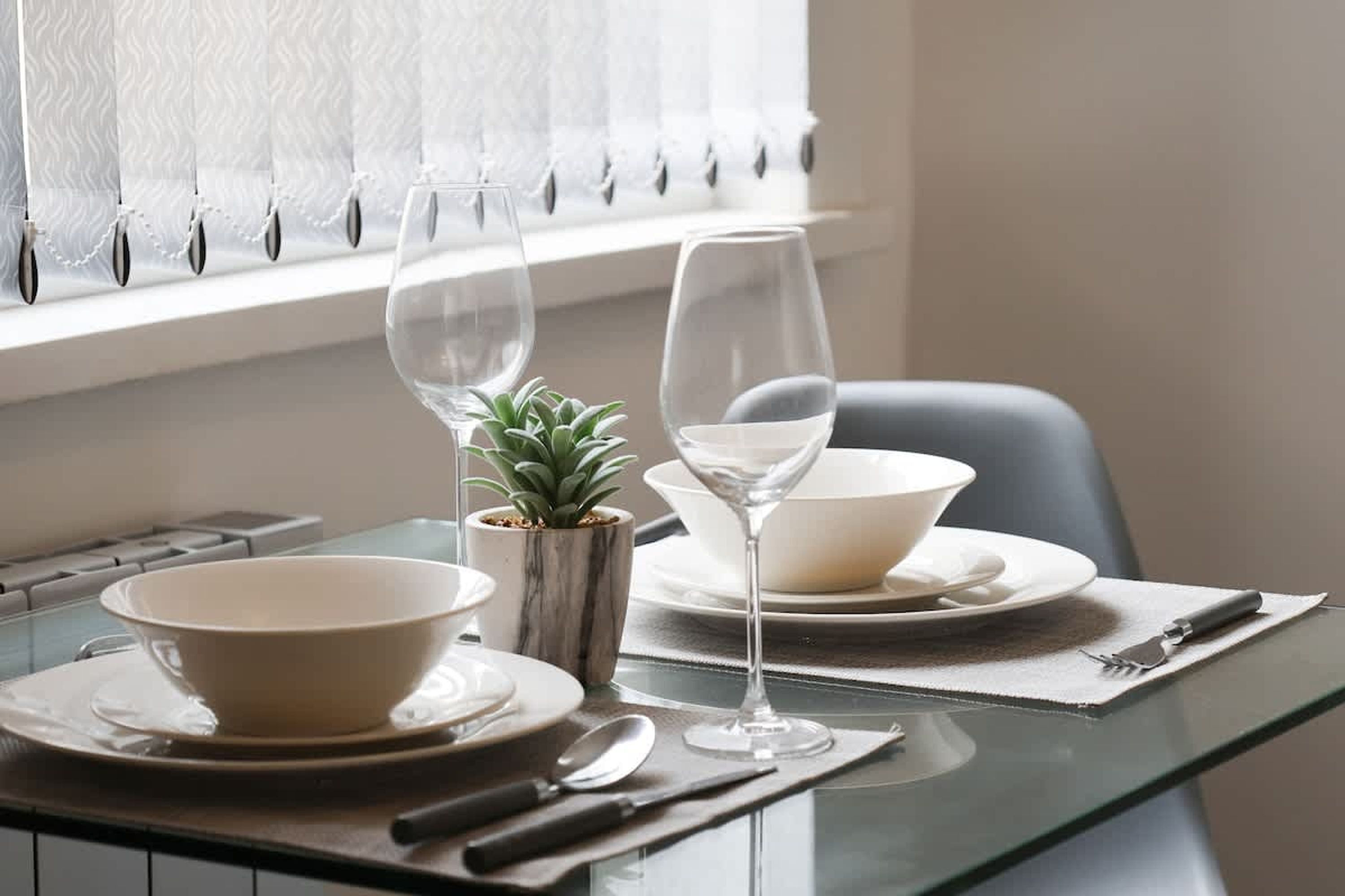 Una mesa de comedor dispuesta con un bol, una copa de vino, una cuchara, un cuchillo y una pequeña planta en maceta.