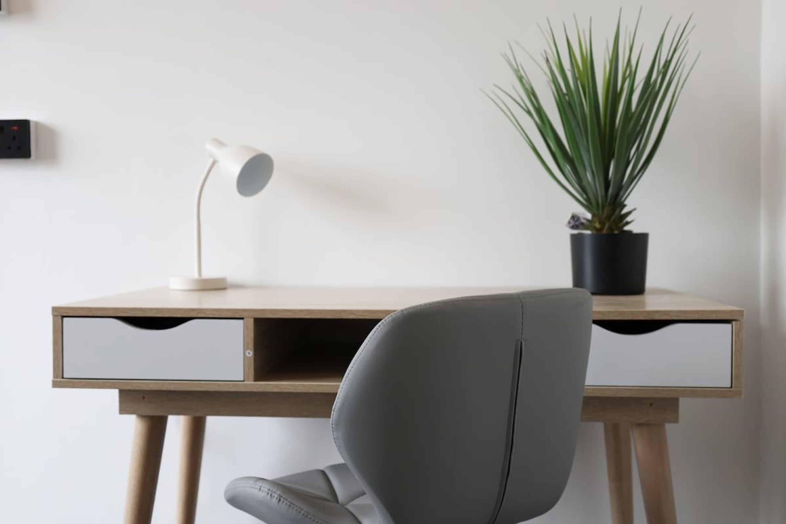 A desk with a lamp, a chair, and a potted plant.