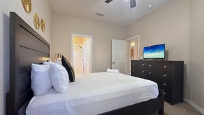 Une chambre à coucher avec un lit, une commode, un ventilateur de plafond et un téléviseur.