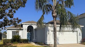 Une maison à deux étages avec un garage, une porte d’entrée et un palmier.