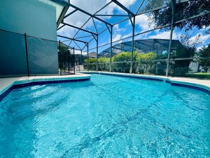 Ein klarer, blauer Pool mit Glasumrandung, umgeben von viel Grün und blauem Himmel.