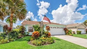 A residential house with a well-maintained lawn, a flag, and various plants.