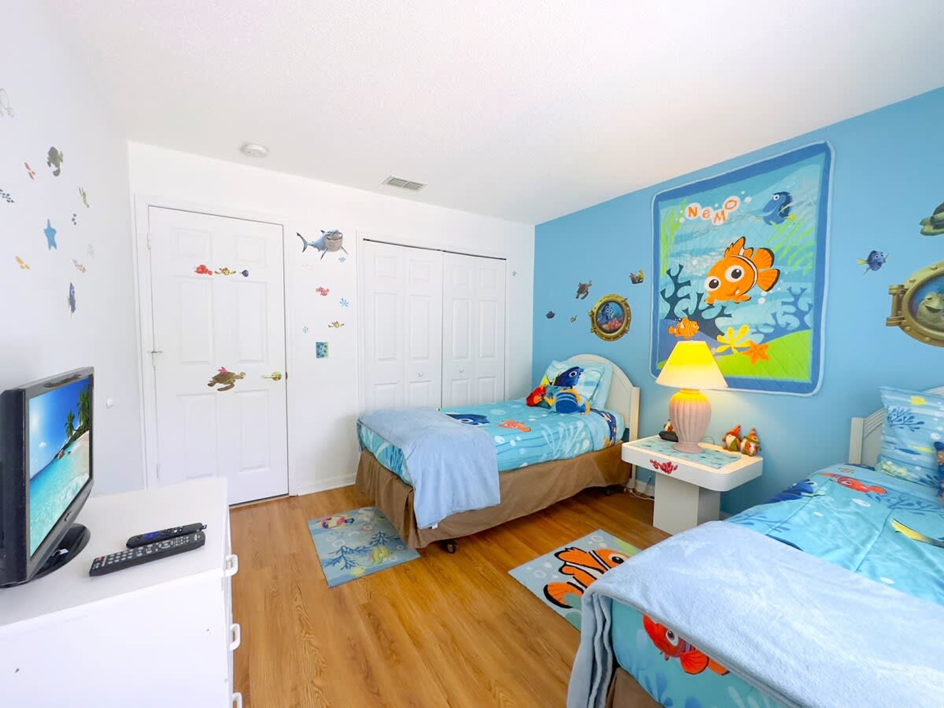 A child's bedroom with two beds, a TV, and a lamp.