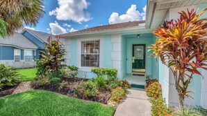 A single-story house with a light blue exterior, a front door, and a small garden with various plants and flowers.