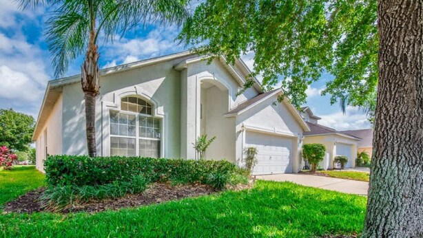 A single-story house with a garage, a well-maintained lawn, and a mature tree. - Villa Near Disney 4 Bd 3 Bt With Private Pool Quiet Comminuty (Davenport)