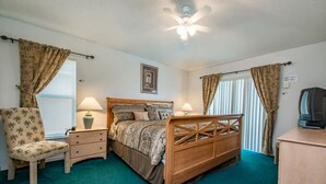 A bedroom with a bed, a chair, a nightstand, a lamp, a ceiling fan, and a television. - Villa Near Disney 4 Bd 3 Bt With Private Pool Quiet Comminuty (Davenport)