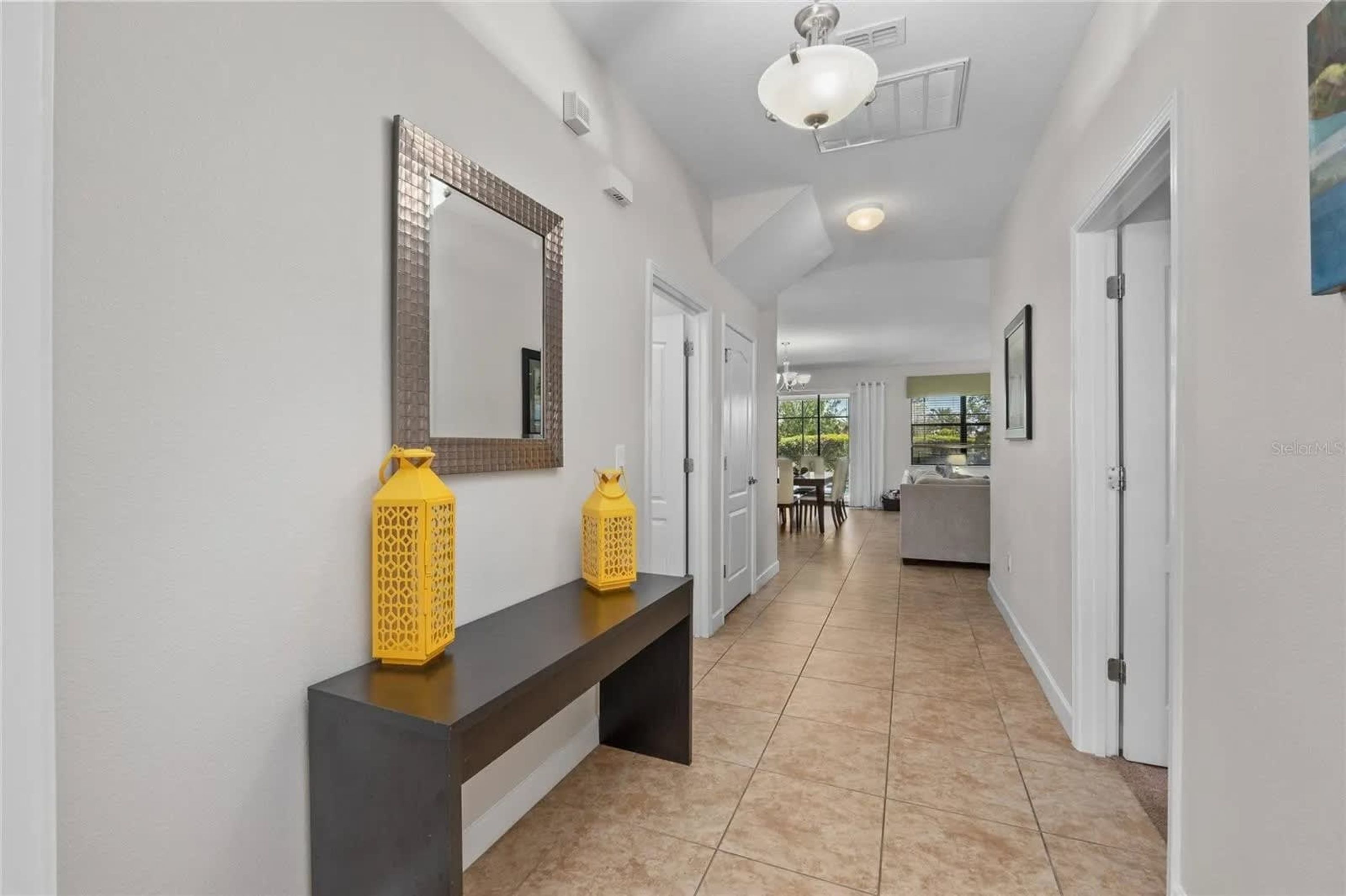 A hallway with a dark console table, two yellow decorative vases, a large mirror, and a ceiling light fixture.