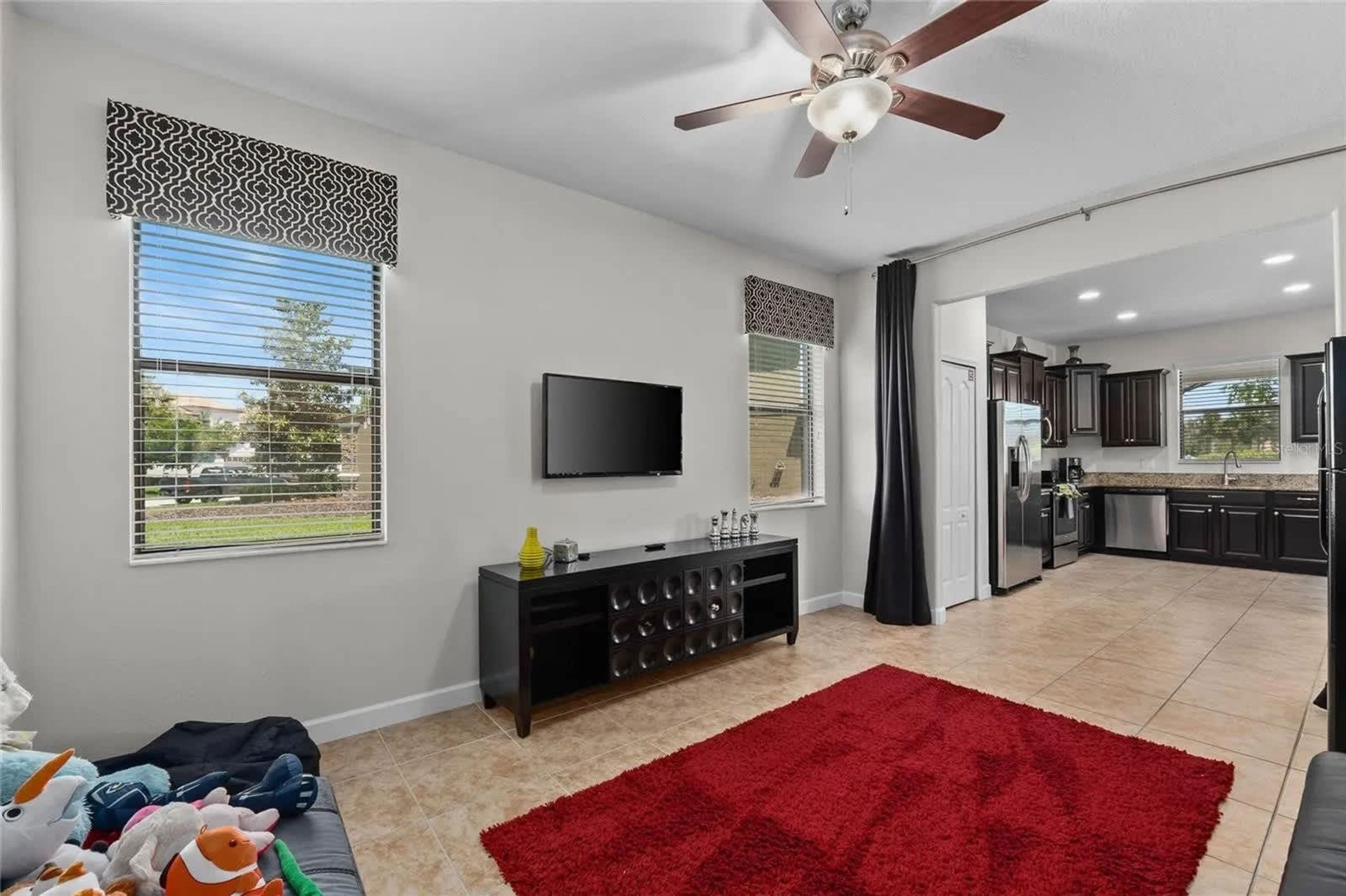 A modern living room with a flat-screen TV, a ceiling fan, and a red rug.