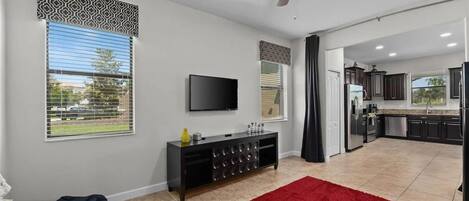 A modern living room with a flat-screen TV, a ceiling fan, and a red rug.