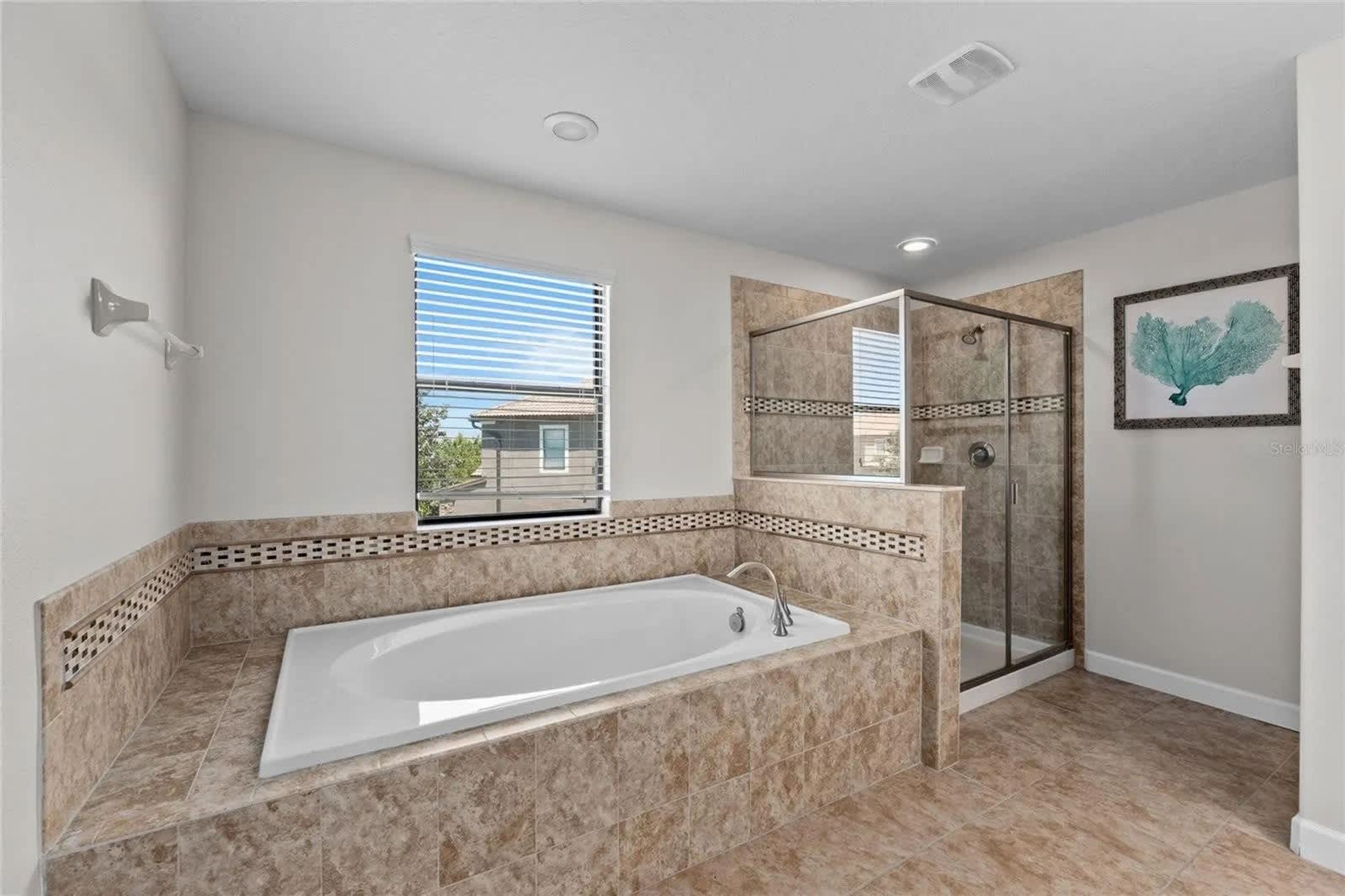 A modern bathroom with a large bathtub, a glass shower enclosure, and a window with blinds.