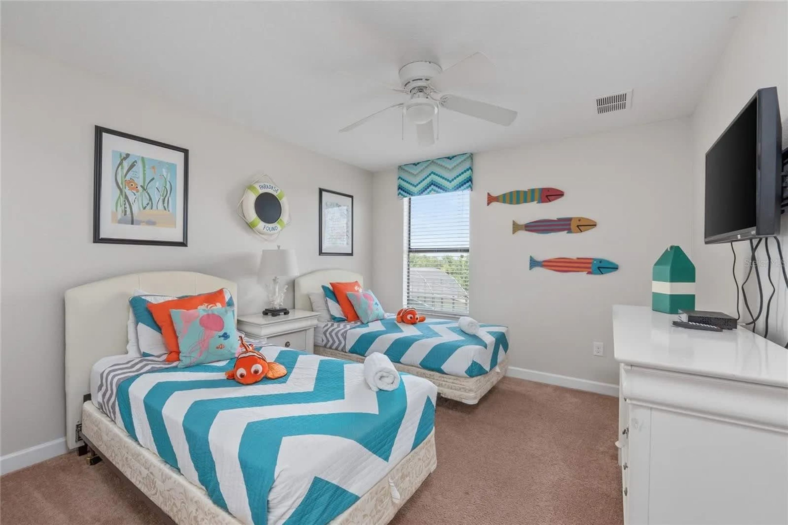 A bedroom with two beds, a ceiling fan, a TV, and wall decorations including fish and a treasure chest.